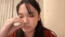 a woman is cleaning her nose with her hand while wearing a red shirt .
