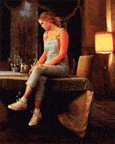 a woman in overalls sits on a table in a room
