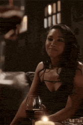 a woman is sitting at a table holding a glass of red wine and a candle .