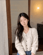 a woman wearing a white sweater and blue jeans stands in a room