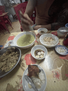 a man is sitting at a table with plates of food and bowls of soup including one that has eggs in it