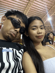 a man wearing sunglasses sits next to a woman wearing a white tank top that says ' i love you ' on it