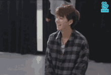 a young man in a plaid shirt is standing in a room with his arms in the air .