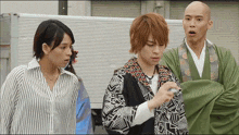 a bald man in a green robe stands next to a woman and a man in a striped shirt