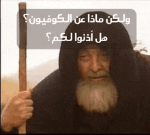 a man with a beard is holding a stick in front of a sign with arabic writing