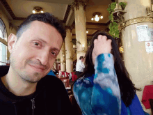 a man and a woman are posing for a picture in a restaurant and the woman is covering her face with her hand