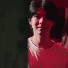 a young man in a white t-shirt is standing in a dark room with red lights behind him .