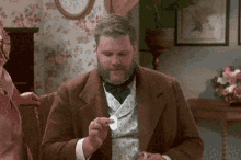 a man with a beard is sitting on a couch and holding a piece of paper in his hand .