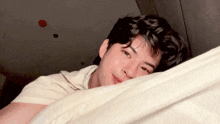 a young man is laying on a bed with his head on a blanket .