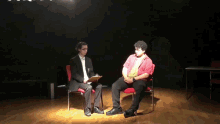 a man in a suit is holding a clipboard while talking to a man in a red shirt