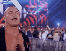 a shirtless wrestler stands in front of a crowd with the hashtag #thekomdreesen on the bottom