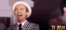 a man wearing a hat and a suit is laughing with his eyes closed .