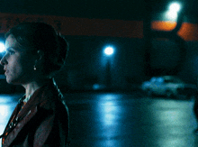 a woman in a red jacket stands in a dark street at night