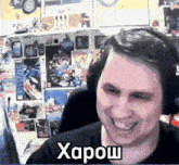 a man wearing headphones is smiling in front of a wall with stickers on it and the word xapow on the bottom