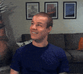 a man wearing a blue shirt is smiling in front of a couch
