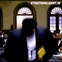a man in a suit is standing in front of a group of people with the website starttamilchat.in written above him