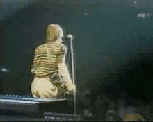 a man in a striped shirt is singing into a microphone on stage