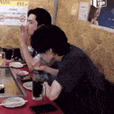 two men are sitting at a table in front of a sign that says ' no smoking '