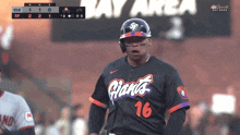 a baseball player wearing a giants jersey stands in front of a scoreboard