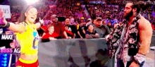 a man and a woman are standing next to each other in front of a crowd in a wrestling ring .