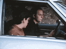 a man is driving a car next to another man who is sitting in the back seat .