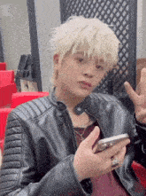 a man wearing a leather jacket is holding a cell phone and giving a peace sign