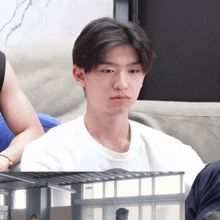 a young man in a white shirt sits on a couch with his eyes closed