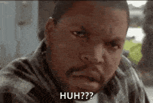 ice cube is wearing a plaid shirt and making a funny face while sitting at a table .