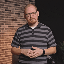 a man wearing glasses and a striped shirt is raising his fist in the air in front of a brick wall