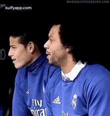 two men are sitting next to each other wearing blue sweatshirts .