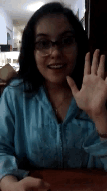a woman wearing glasses and a blue shirt is waving at the camera