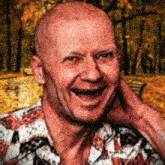 a bald man in a floral shirt is smiling with his hand behind his head