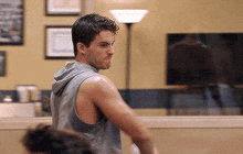 a man in a grey tank top is standing in a room