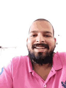 a man with a beard wearing a pink polo shirt is smiling
