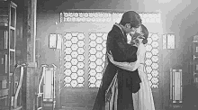 a black and white photo of a man kissing a woman in a room .