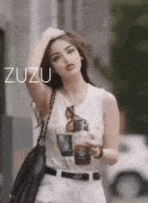 a woman in a white tank top and white shorts is holding a cup of coffee and a black purse .