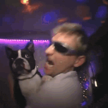 a man wearing sunglasses is holding a small dog