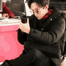 a man wearing sunglasses is kneeling down while looking at his phone .