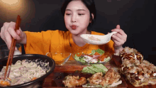 a woman in an orange shirt is eating a salad with chopsticks