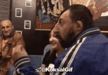 a man with a beard is sitting next to a woman in a room with other people .