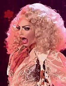a drag queen with pink hair is making a funny face with her tongue out .