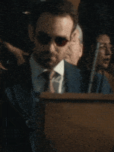 a man in a suit and tie stands behind a podium in front of a crowd