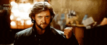 a man with a beard is standing in a room with his fist up .