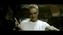 a man in a white shirt is holding a pencil in his mouth and looking at the camera .