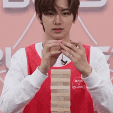 a young man in a boys ii planet shirt holds a stack of wooden blocks in his hands