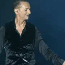 a man wearing a black vest and a black shirt is standing on a stage