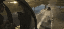 a man in a helicopter looks out the window at a boat going down a river