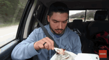 a man in a car eating a cinnamon roll with a subscribe button on the bottom right