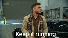 a man with a scarf around his neck is standing in front of a car that says " keep it running "