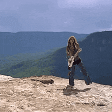 a woman playing a guitar on top of a rocky cliff